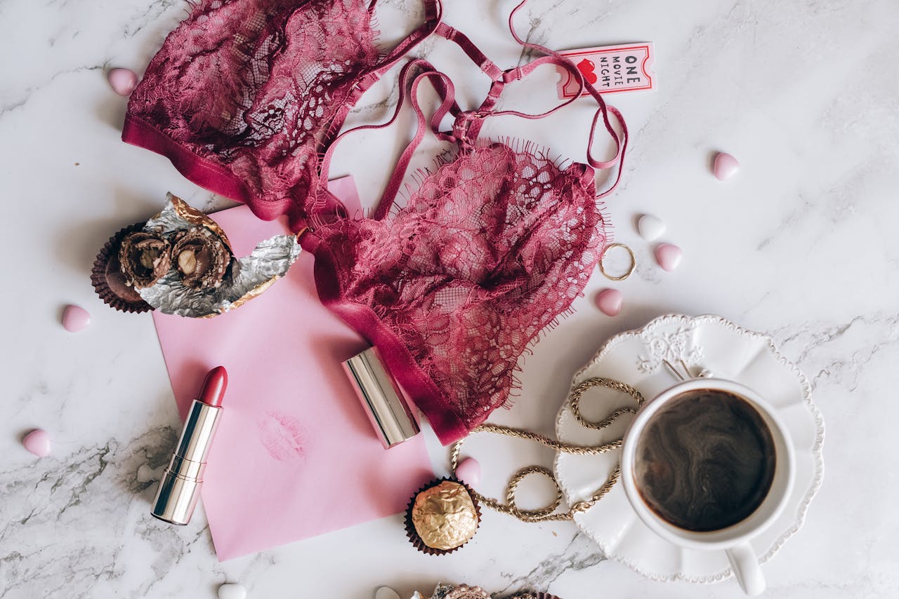 A romantic flat lay with lace lingerie, coffee, chocolates, and a lipstick on a marble surface.